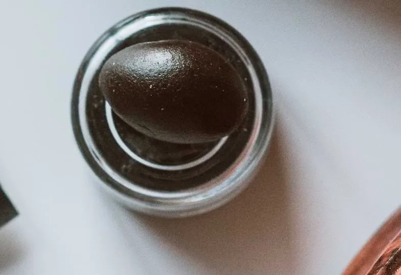 Boulette ovoïde de haschich brun foncé placée dans un petit pot en verre transparent vue du dessus sur surface claire