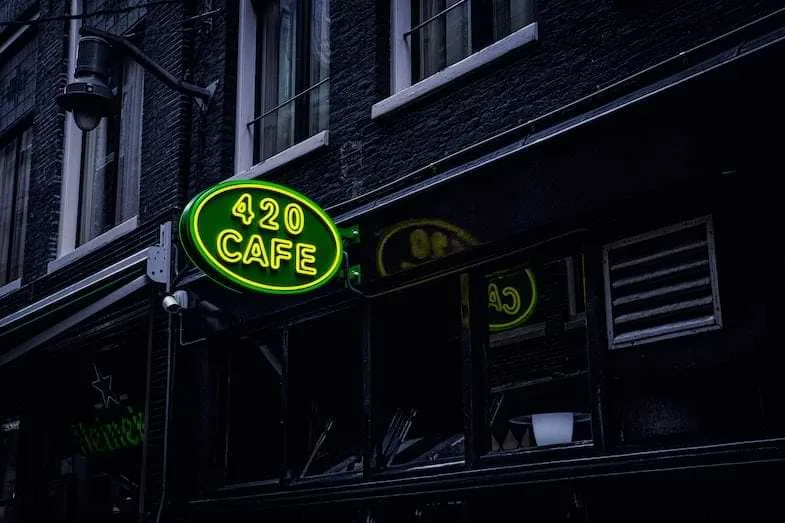 Enseigne au néon vert et jaune "420 Cafe" sur la façade sombre d'un établissement à Amsterdam, emblème culturel du quartier cannabique
