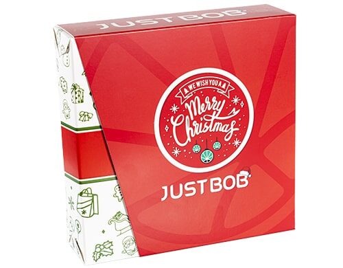 Boîte Justbob XMAS KIT en rouge et blanc avec le message 'Nous vous souhaitons un Joyeux Noël' et le logo de la feuille de cannabis, présentant un emballage festif pour cadeaux de weed CBD