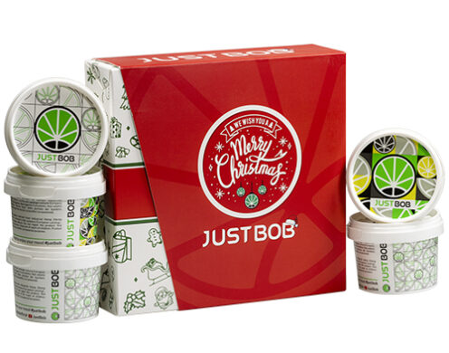 Boîte ouverte Justbob XMAS KIT avec plusieurs contenants de fleur de CBD légale, présentant la marque de Noël et le design de feuille de cannabis, parfait pour les cadeaux des fêtes