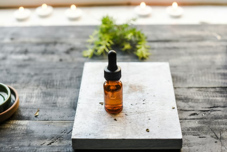 bouteille d'huile de cbd sur une table en bois avec une feuille de cannabis en arrière-plan | Justbob