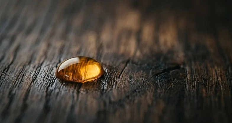 Goutte d'huile CBD ambrée sur surface en bois foncé illustrant les extraits de cannabidiol issus de variétés californiennes disponibles en France