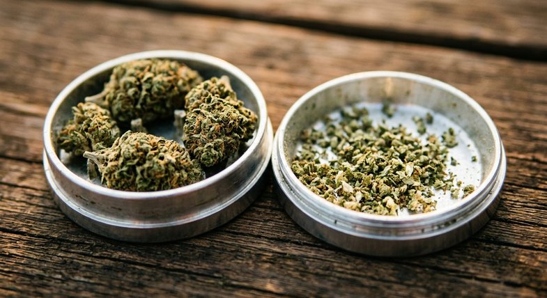 Gros plan macro d'un grinder en aluminium poli ouvert en deux moitiés avec des fleurs séchées de chanvre CBD et particules à l'intérieur, sur table en bois sombre