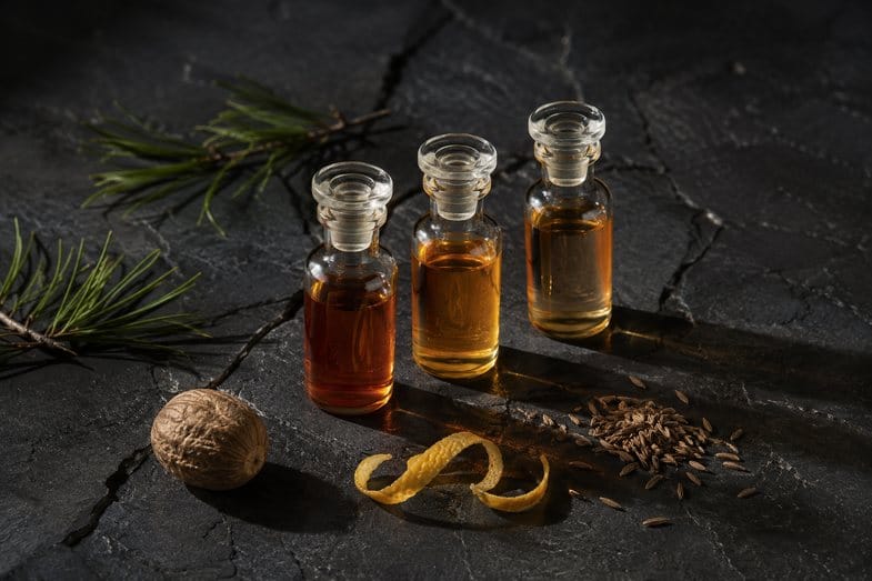 Fioles aromatiques et épices sur ardoise Trois fioles de verre bouchées, remplies de liquides ambrés, posées sur une dalle d'ardoise noire fendue avec pin, muscade, zeste et graines